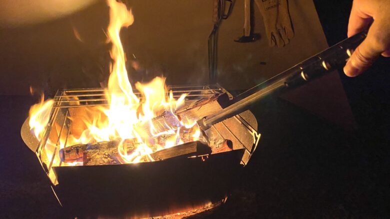 薪バサミで焚火中の薪を挟む